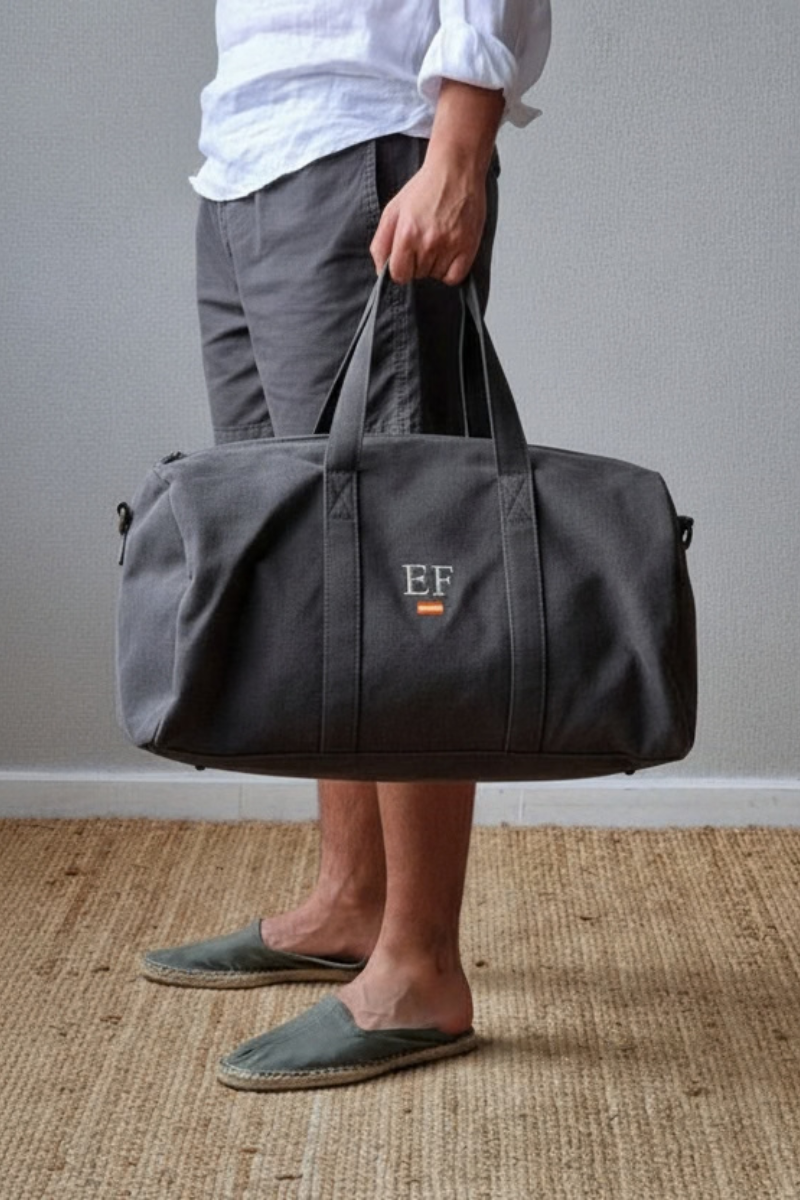 Bolso de fin de semana unisex en gris oscuro con opción de personalización. Cierre cremallera, bolsillo interior y asa ajustable. Ideal para viajes y escapadas. Envío 24h.